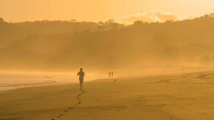 Fototapeta na wymiar Unrecognizable sporty female person jogging in golden sunlight at Playa Venao