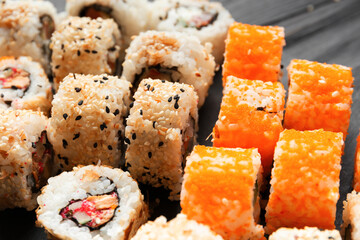 Set of various sushi rolls on a black slate plate, close-up.