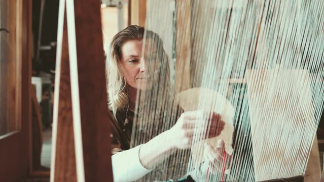 Crafty woman weaving at a loom at her workshop
