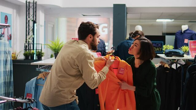 Frustrated customers fighting in store, pushing clothing item in different directions. Black friday shopping madness with two shoppers arguing in modern fashion outlet, bargain hunting.