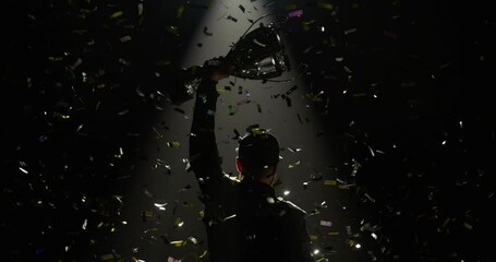 Silhouette of race car driver celebrating the win in a race against bright stadium lights, rising a trophy over his head - Powered by Adobe