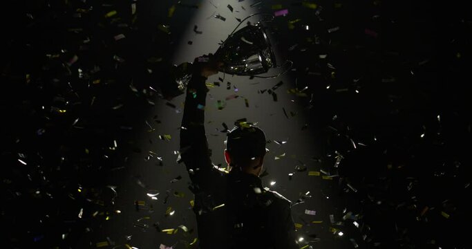 Silhouette of race car driver celebrating the win in a race against bright stadium lights, rising a trophy over his head