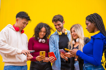 Low angle view of a group of smiling young multi ethnic teenage friends using cell phones on a...
