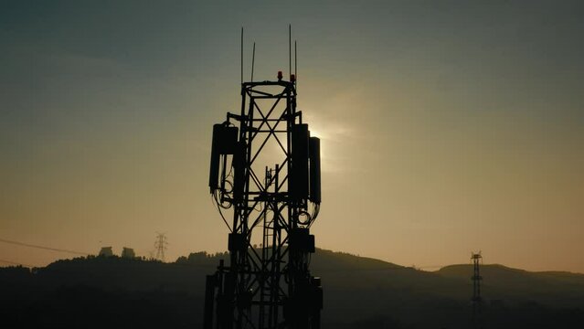 4K drone footage of cellular base station of cell tower. Aerial filming of telecom antenna and telephone mast against sun with transmission towers in the background during golden hour stock video.