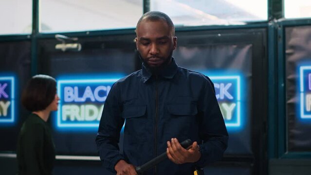 Security guard in clothing store wearing uniform and presenting on duty at black friday promotional event. Shopping center protective agent with security baton ensuring safety.