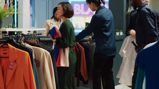 Crazy man shopping on black friday, bringing huge rack of clothes at cash register counter for checkout. Shopper couldnt decide on clothing items, buying whole fashion collection. Handheld shot.