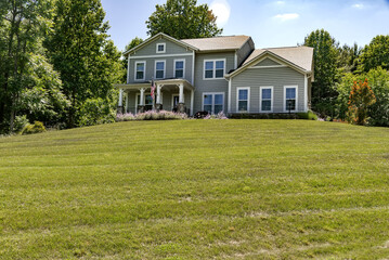 beautiful house with gray siding on the edge of the forest. Large lawn and green trees.