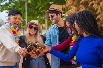 Obraz premium Group of multi ethnic friends at a party in a park having fun - Diverse young people toasting with glass bottles of beer at a summer party, youth concept