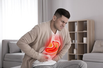 Man suffering from heartburn at home. Stomach with hot chili pepper symbolizing acid indigestion,...