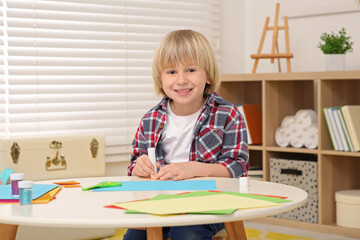 Cute little boy with glue stick at desk in room. Home workplace