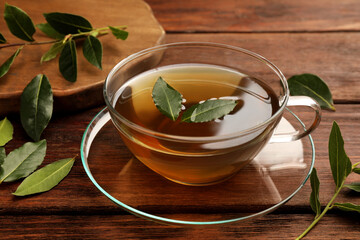 Cup of freshly brewed tea with bay leaves on wooden table, closeup