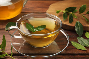 Cup of freshly brewed tea with bay leaves on wooden table, closeup