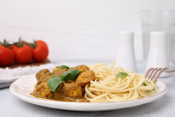 Delicious chicken, pasta with curry sauce and basil served on white table, closeup
