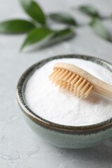 Fototapeta na wymiar Bamboo toothbrush and bowl of baking soda on light gray table, closeup