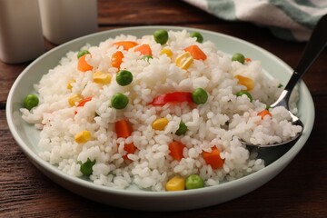 Delicious rice with vegetables served on wooden table, closeup