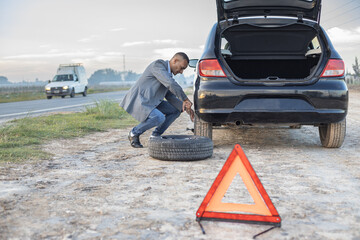 Latino man changes a flat tire on his car at the side of the road.