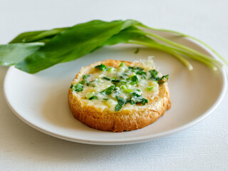Delicious toasted bread with chopped green wild leek and cheese on plate with ramson leaves, close up