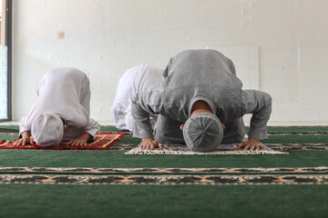 Asian muslim family praying salah jamaah together at home in sujud or prostration posture, one of...