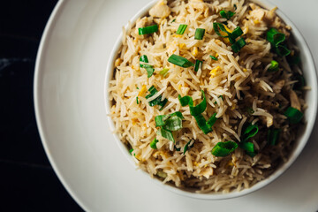 Fried white rice with green onion and egg in a white round plate on a white platter. Close-up