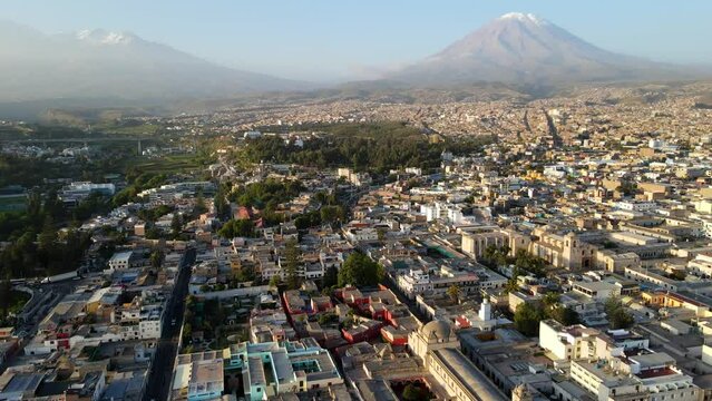 Aerial shot drone flies to right over Arequipa with Misti Volcano and Chachani Volcano at dusk in the distance