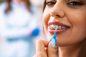Young Charismatic woman using interdental brush for cleaning dental braces, doctor in the...