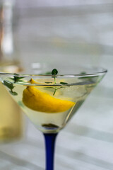 summer cocktail with lemon, mint and ice cubes in a transparent martini glass on a light background