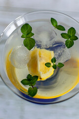 summer cocktail with lemon, mint and ice cubes in a transparent martini glass on a light background