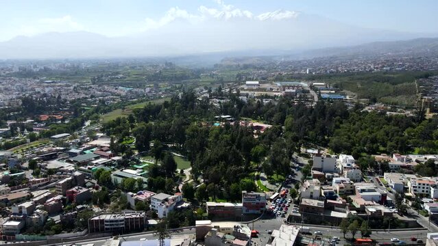 Aerial shot drone flies to the right over city with Chachani volcano in the distance