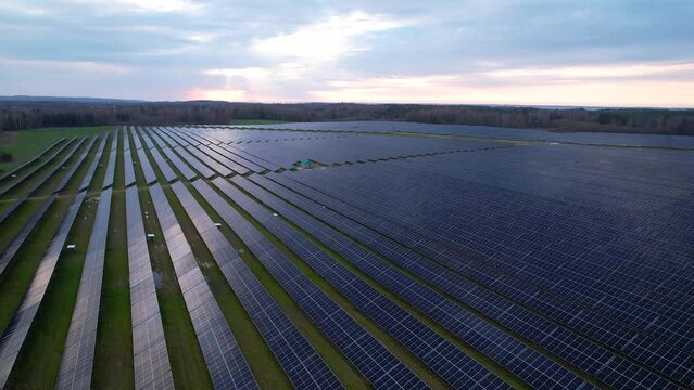 Vast solar farm with long rows of solar PV panels, aerial pullback view
