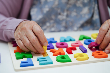 Asian elderly woman playing puzzles game to practice brain training for dementia prevention, Alzheimer disease.