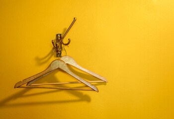 Two empty wooden clothes hangers without shirts or dress hanging on a hook on yellow wall...