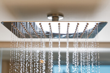 Water flows from the tropical shower. Large water consumption. Chrome large shower head, modern design. Water flowing from the square shower head in a modern bathroom.