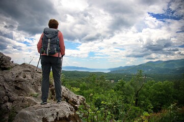 Rear view of senior woman standing at the edge of a cliff in the mountains