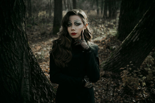 A young woman in a Gothic gloomy image of a witch in a forest. Halloween costume.