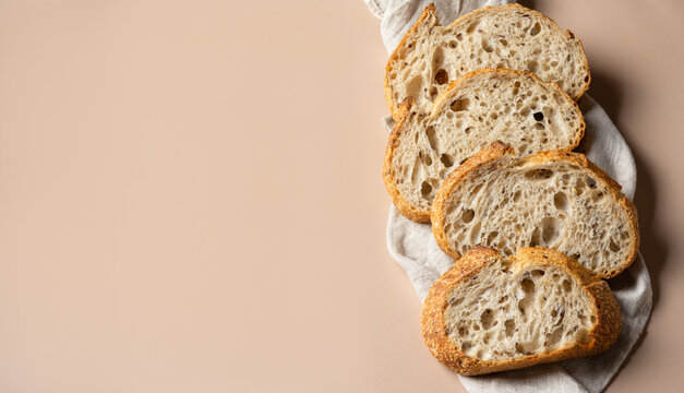 Sliced sourdough bread on a linen towel. Fresh homemade artisan bread, organic bakery products. Banner with copy space on beige background.