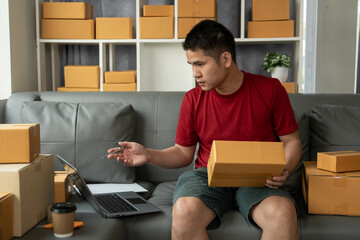 Happy asian man customer opening cardboard box parcel on sofa.