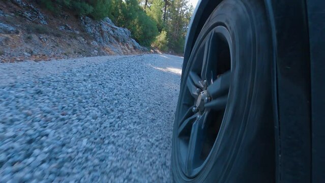 Close up of the rear wheel of the car. Dust and stones fly out of it. The camera is mounted on back of car. The car is driving on an asphalt and gravel road. The work of car's suspension can be seen