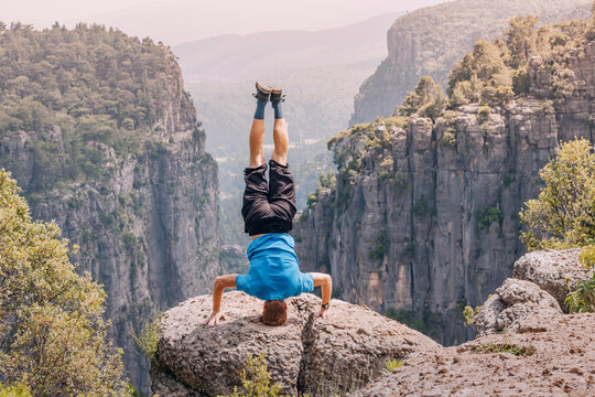 Man standing on his head on the edge of a big cliff with view of canyon Tazi in Turkey. Yoga pose concept