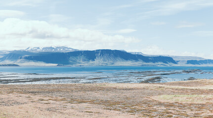 vue sur une plage avec un cours d'eau et une montagne en arrière plan lors d'une journée d'été ennuagée