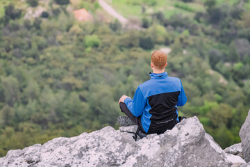 Naklejka premium Man meditating in lotus yoga pose on top of the mountain cliff overlooking scenic view