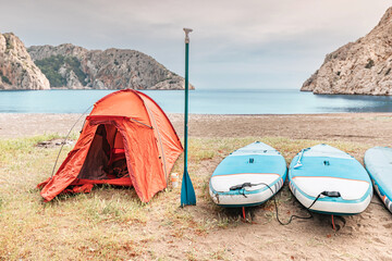 Camping tent with sup boards on the wild beach at mediterranean seacoast. Water trip and sportive...