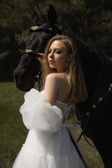 Beautiful caucasian girl in a wedding dress next to a horse looks at the camera