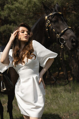 Beautiful caucasian brunette girl in a wedding dress next to a horse