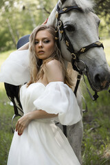 Beautiful Caucasian blonde girl in a wedding dress in the forest next to a horse. Idea for wedding photography.