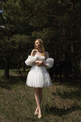 A beautiful caucasian girl in a wedding dress stands in the forest under the sunlight