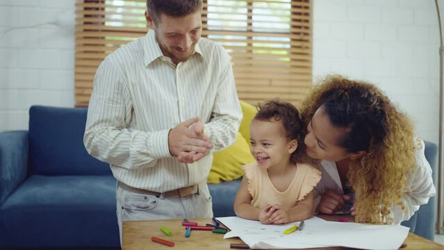 Dad, Mom and little daughter drawing with colorful pencils on paper happy smiling.Young family spend free time together in living room at home.