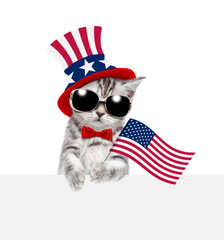 Cute kitten wearing like Uncle Sam looks above empty white banner and holds USA flag. isolated on white background