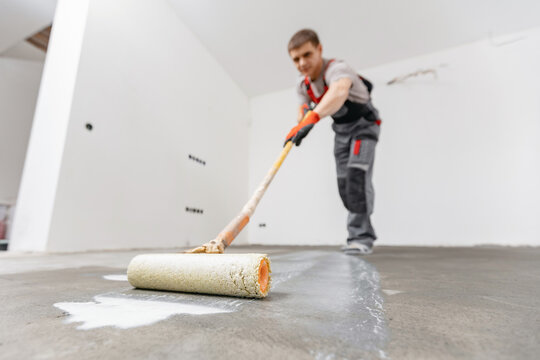 Floor priming process. Worker use primer on concrete floor before laying tiles, strengthening surface