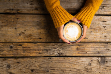 Cropped hands of caucasian woman wearing yellow sweater holding coffee cup over wooden table