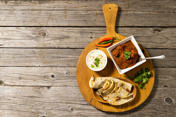 Flatbread with meat gravy and rice in bowls with cilantro and chili on serving board over table